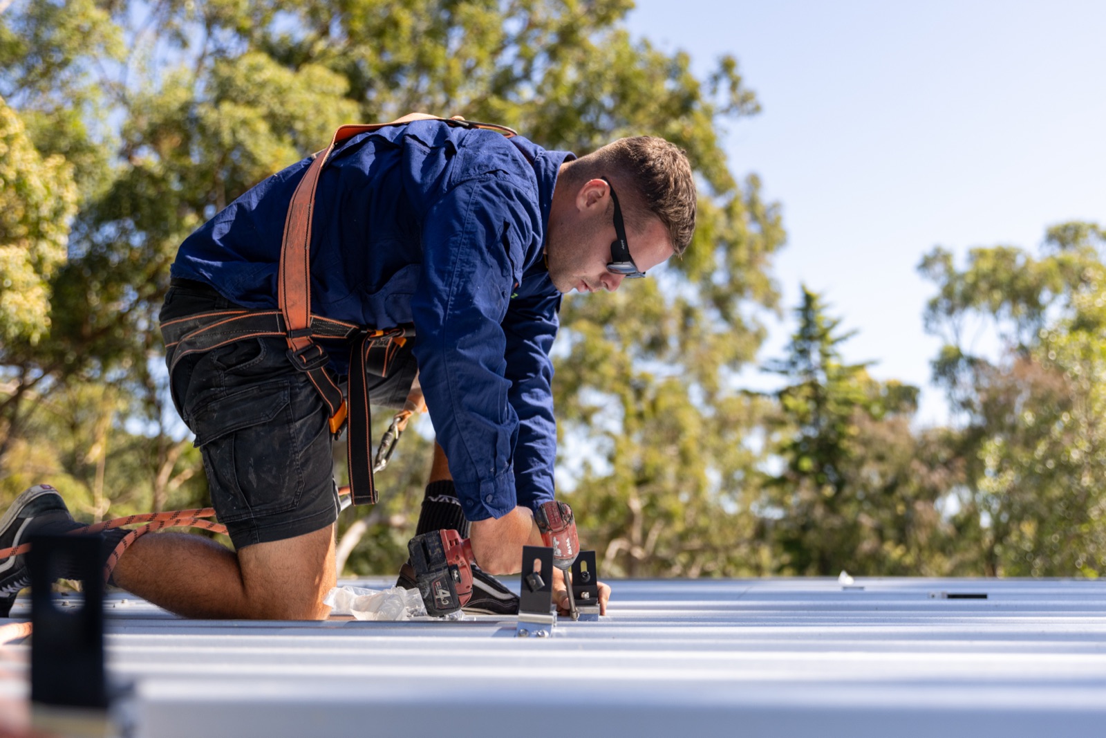 Solar installer drilling roof mounts on a metal roof